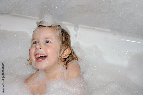 Kid having fun in the bath with bubbles. Happy child enjoying bath time. Little girl smiling in the bath with soap foam