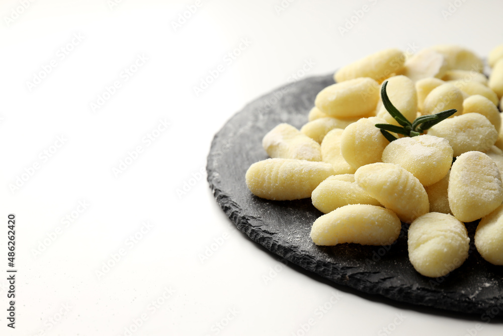 Slate board with raw potato gnocchi on white background