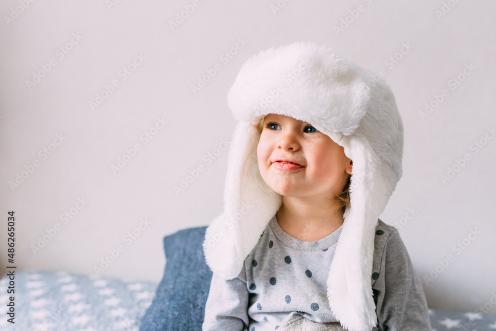 Cute child y on the bed in cozy adult clothes and a hat with earflaps. Cute child y on the bed in cozy adult clothes and a hat with earflaps.