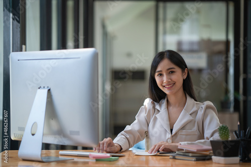 Young beautiful Asian businesswoman working on her project with computer and smiling at the camera