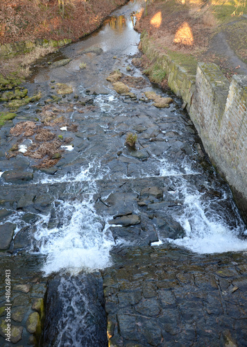 The dam of the breeding fish pond has a canal safety overflow similar to a weir. the water flows under a stone bridge with several arches. bridge on crown of dam with a wooden railing in silhoulete photo