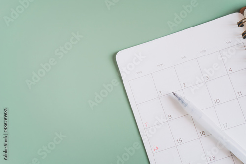 white pen on blank white planner  on green background, top view for timeline, schedule, routine work concept photo