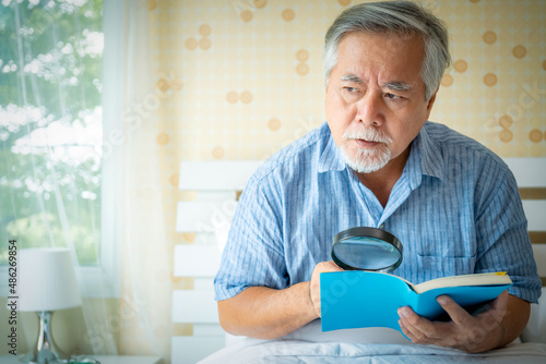 Portrait old elderly casual male or Senior man with eyeglasses reading book in bedroom at home, Mature man lifestyle concept.