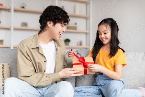 Satisfied japanese millennial father receives gift from teen daughter open box with gift in living room interior photo