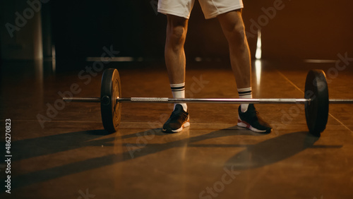 Cropped view of sportsman standing near barbell on dark background