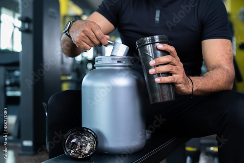 Fotografie close up shot of bodybuilder hands taking protein powder and mixing with water on bottle by shaking at gym - concpet of muscular gain, nutritional supplement and wellness