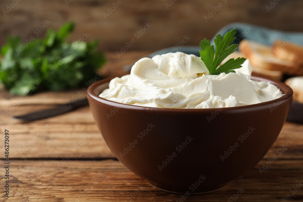 Bowl of tasty cream cheese and parsley on wooden table, closeup Bowl of tasty cream cheese and parsley on wooden table, closeup