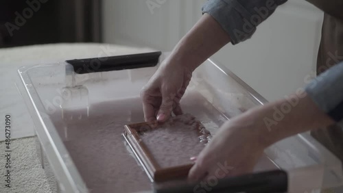 A woman holding a frame for making paper sheets from recycled paper. Selective focus. Household hobby, paper recycling. The concept of zero waste, recycling, ecology
