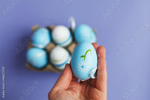 womans hand holding easter colorful handmade painted blue eggs in a box on purple background