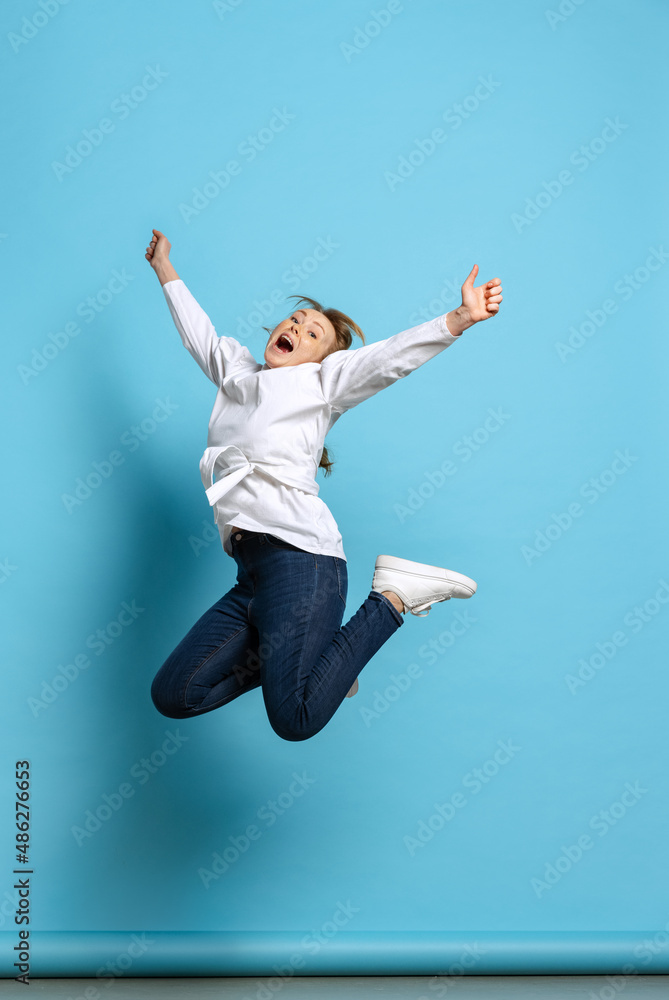 Full-length portrait of excited young girl jumping isolated on blue background. Concept of wow emotions, facial expressions, ad, sales