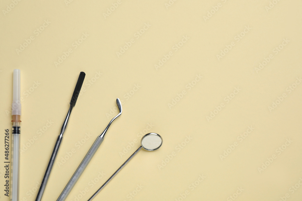Set of dentist's tools and syringe on pale yellow background, flat lay. Space for text Set of dentist's tools and syringe on pale yellow background, flat lay. Space for text