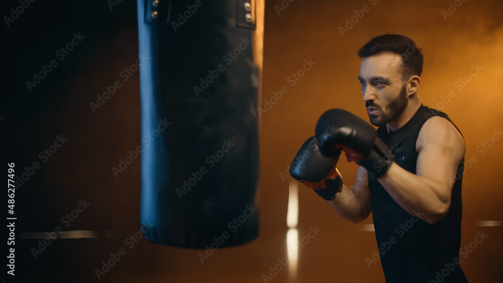 Athletic boxer training with punch bag on dark background