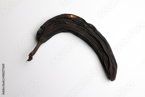 An isolated completely blackened, overripe rotten banana on a white background. Color abstract photo for artistic design poster or illustration of fruit ripening. 