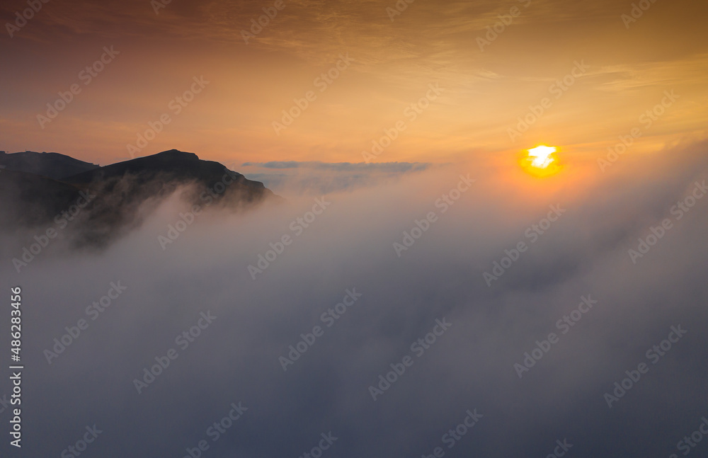 Sunrise over the sea of clouds on top of the mountains. Aerial view with amazing sky color.