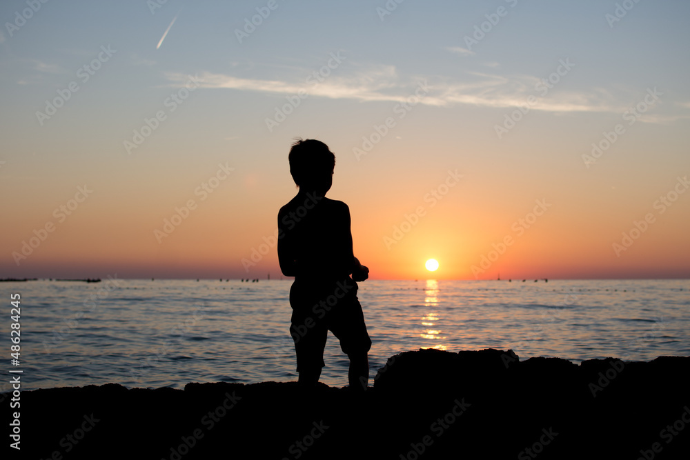 Silhouette of a person on the beach at sunset. Kid and vacation concept.