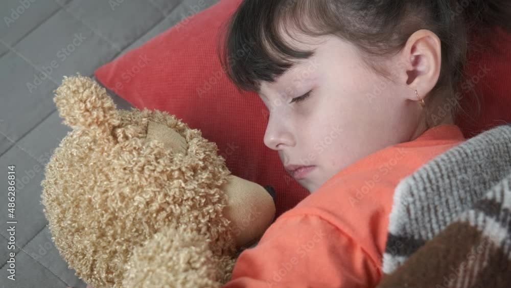 Teddy bear by sleeping child. A view of teddy bear under the blanket with sleeping child in the room. Teddy bear by sleeping child. A view of teddy bear under the blanket with sleeping child in the room.