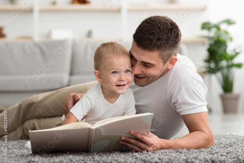 Portrait Of Caring Young Dad Reading Book To Happy Baby At Home