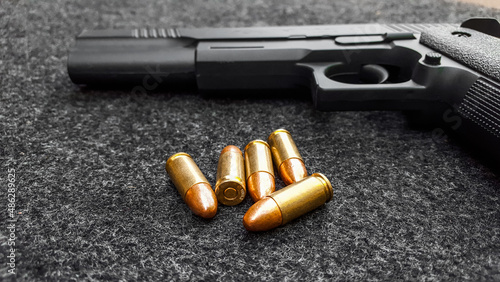 Black artificial handgun and bullets on dark gray fabric. Concept for security of social, personal and shooting sport equipments