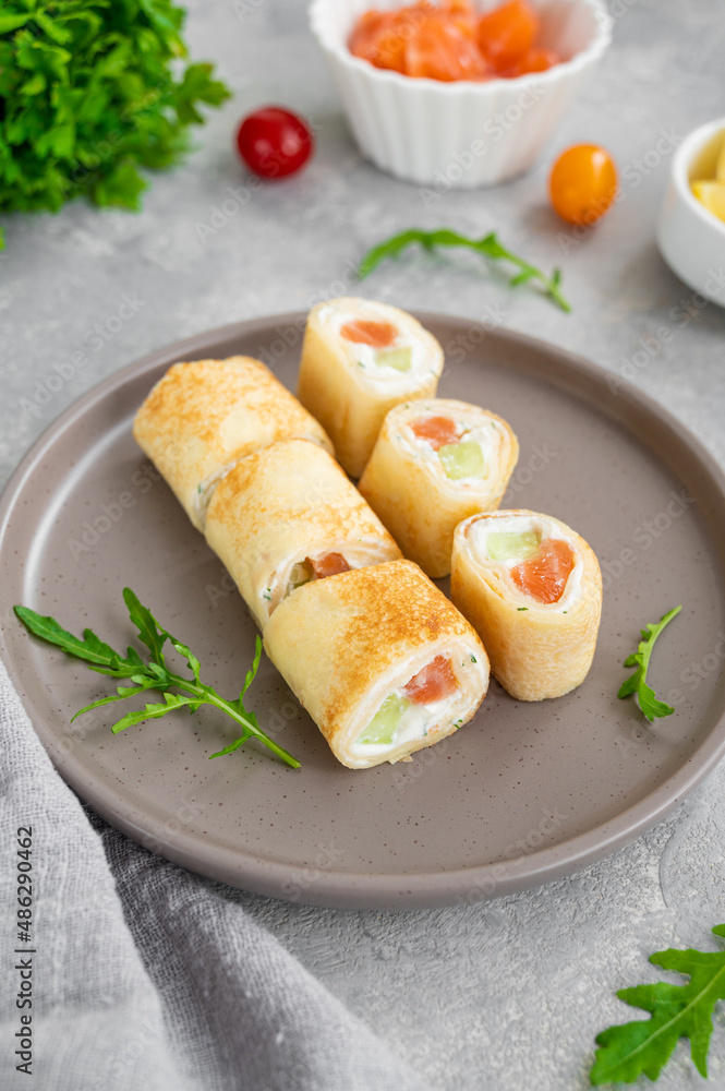 Thin pancake rolls or crepes rolls with smoked salmon, cream cheese, cucumber and dill on a gray concrete background. Selective focus. Thin pancake rolls or crepes rolls with smoked salmon, cream cheese, cucumber and dill on a gray concrete background. Selective focus.