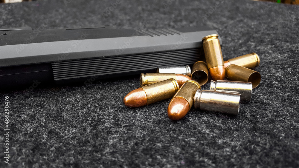 Black artificial handgun and bullets on dark gray fabric. Concept for security of social, personal and shooting sport equipments Black artificial handgun and bullets on dark gray fabric. Concept for security of social, personal and shooting sport equipments