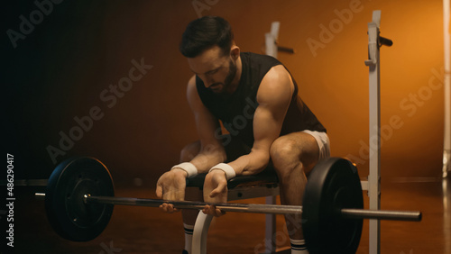 Muscular man training with barbell on flat bench on dark background