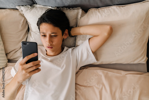 Asian boy using mobile phone while sitting on bed