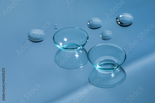 Contact lenses and drops of water on light blue reflective surface