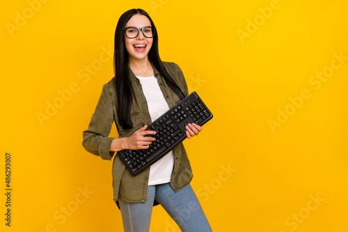 Photo of clever young lady hold keayboard wear eyewear khaki shirt jeans isolated on yellow background photo