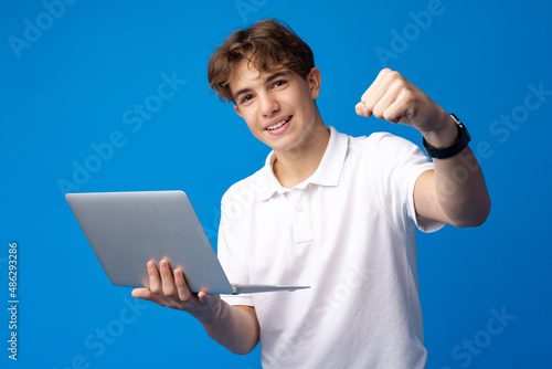 Teenage boy using laptop against blue background