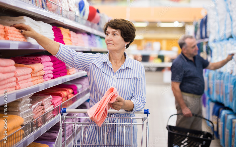 elderly retired senora buying pink towels in linen section of supermarket