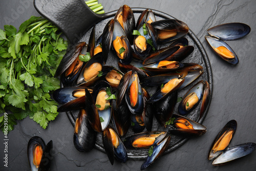 Serving board with cooked mussels and parsley on slate table, flat lay photo