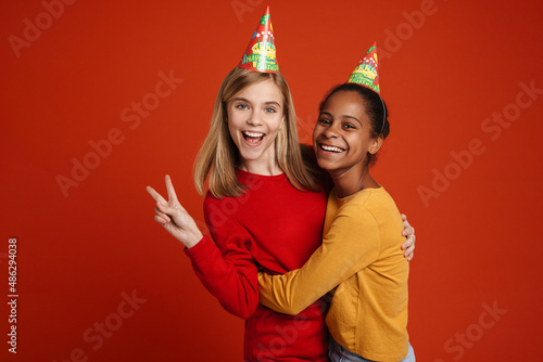 Multiracial girls wearing party cones gesturing while hugging together