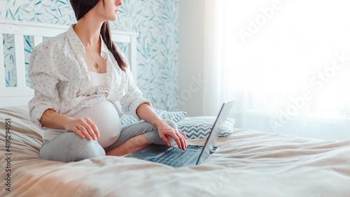 Pragnant woman with laptop on bed. Pregnant working at home.
