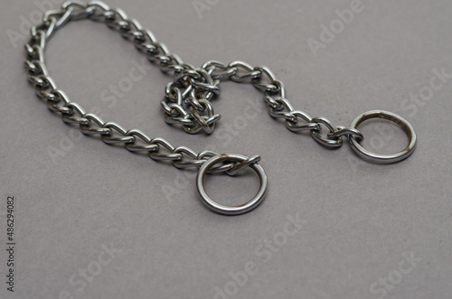 Silver metal chain with two rings on a gray background. Tugging