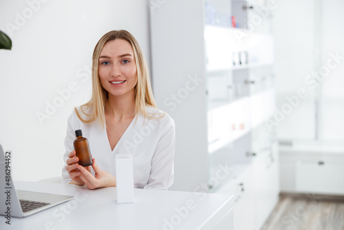 Cheerful woman beautician demonstrating cosmetic lotion at work