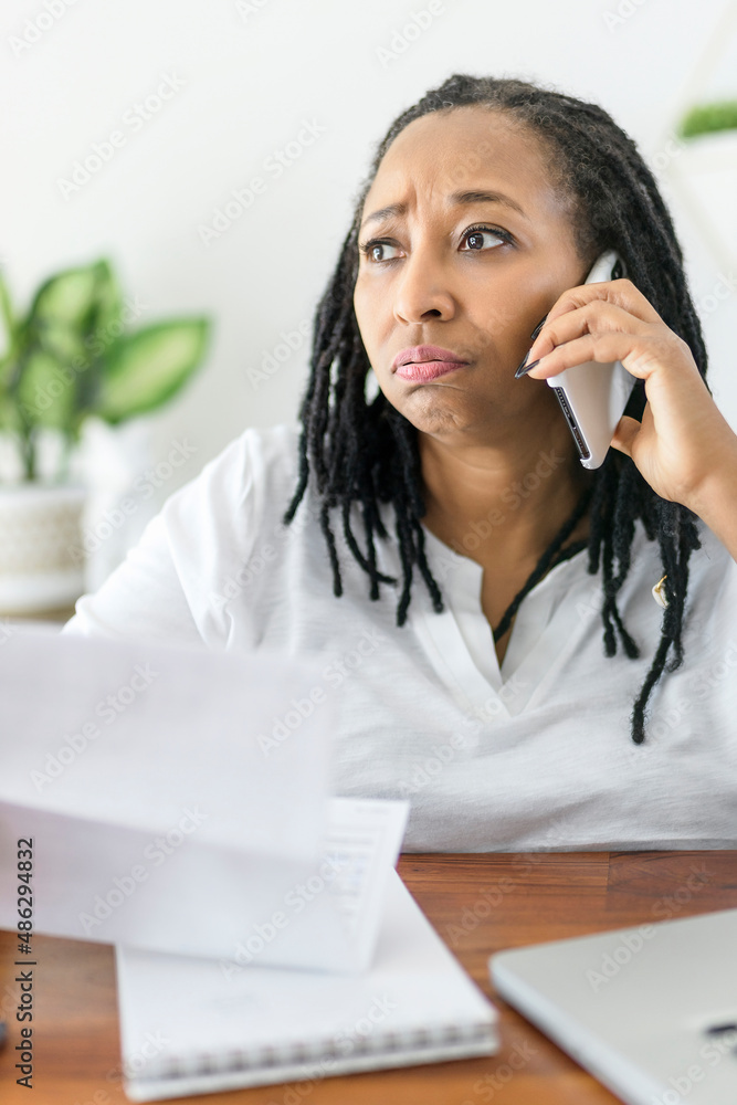 black woman using computer in modern kitchen interior with cellphone on ear black woman using computer in modern kitchen interior with cellphone on ear