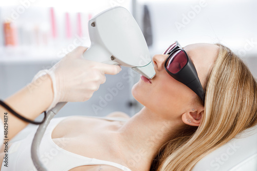 Blonde woman receiving laser hair removal treatment in beauty salon photo