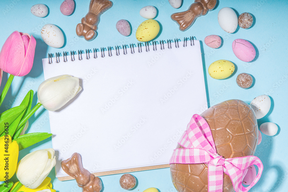 Easter holiday greeting card background, with chocolate easter bunny, eggs, and tulip flowers, on light blue background flatlay frame copy space top view