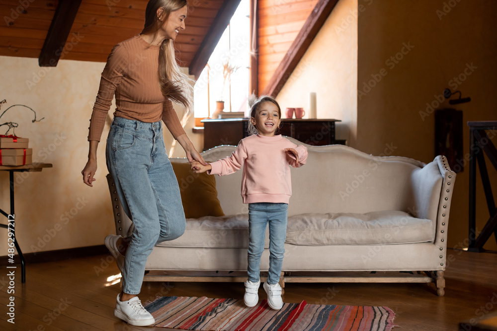 Positive mother dancing to music and jumping with little girl