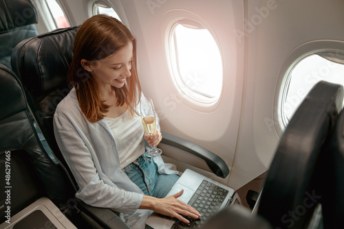 Smiling woman using laptop and drinking champagne in plane