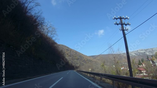 Slow car or a motorcycle ride on a mountain road, passing by a mountain village. Autumn, blue clear sky. POV shot photo