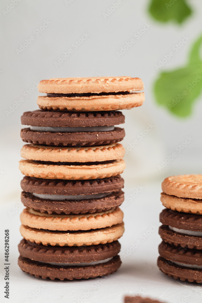 Stack of milk and chocolate cookies with cream filling close up on a white table. Bakery products concept. Stack of milk and chocolate cookies with cream filling close up on a white table. Bakery products concept.