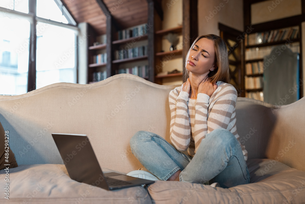 Tired woman sitting on couch with pc, massaging neck Tired woman sitting on couch with pc, massaging neck