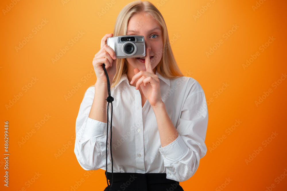 Beautiful teen girl with old photo camera against orange background