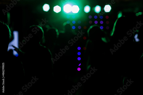 cheering crowd in front of bright blue green stage lights. Silhouette image of people dance in disco night club or concert at a music festival.
