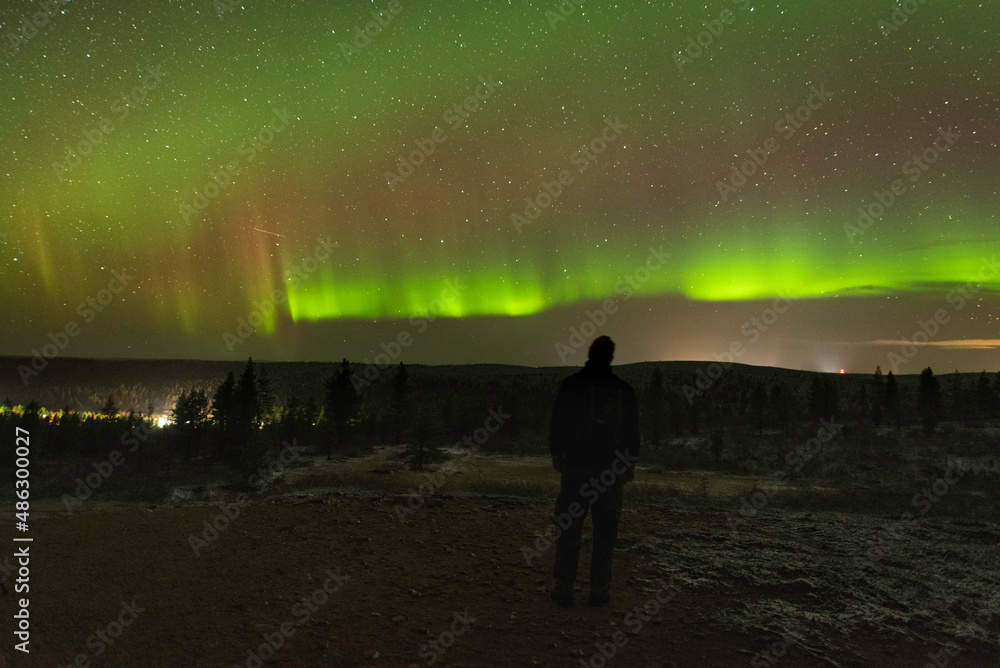 Figure in the dark observing night sky with green and purple aurora colors in the sky above the horizon