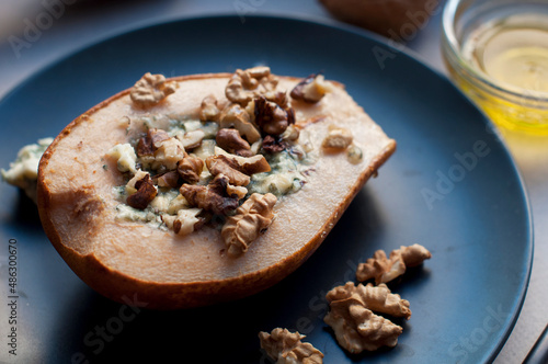 Pear baked with dorblu cheese, honey and walnuts on a black plate on a gray background.