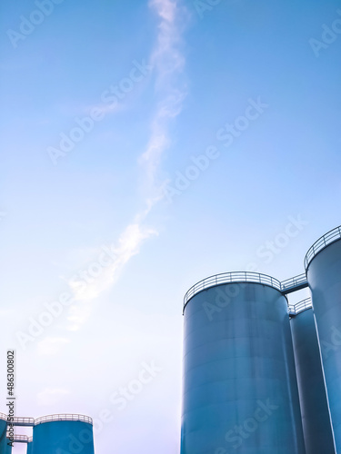 Low angle view of storage fuel tanks inside of petroleum industrial area against blue sky in evening time