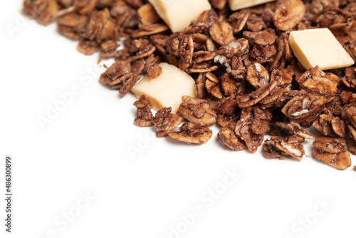 Granola with white chocolate pieces. Large amount of chocolate covered baked rolled oats clusters, randomly placed. Cereal background or healthy snack texture. Isolated on white. Selective focus.