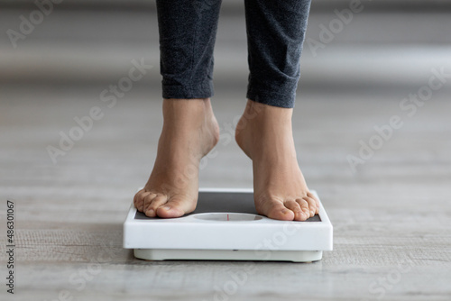 Unrecognizable young Indian lady checking her weight, standing on scales indoors, closeup of feet